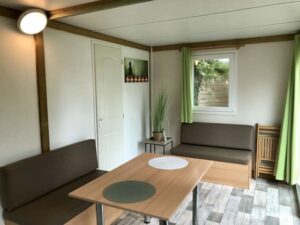 Intérieur lumineux d'un hébergement avec table, banquettes marron, rideaux verts et décoration zen épurée.